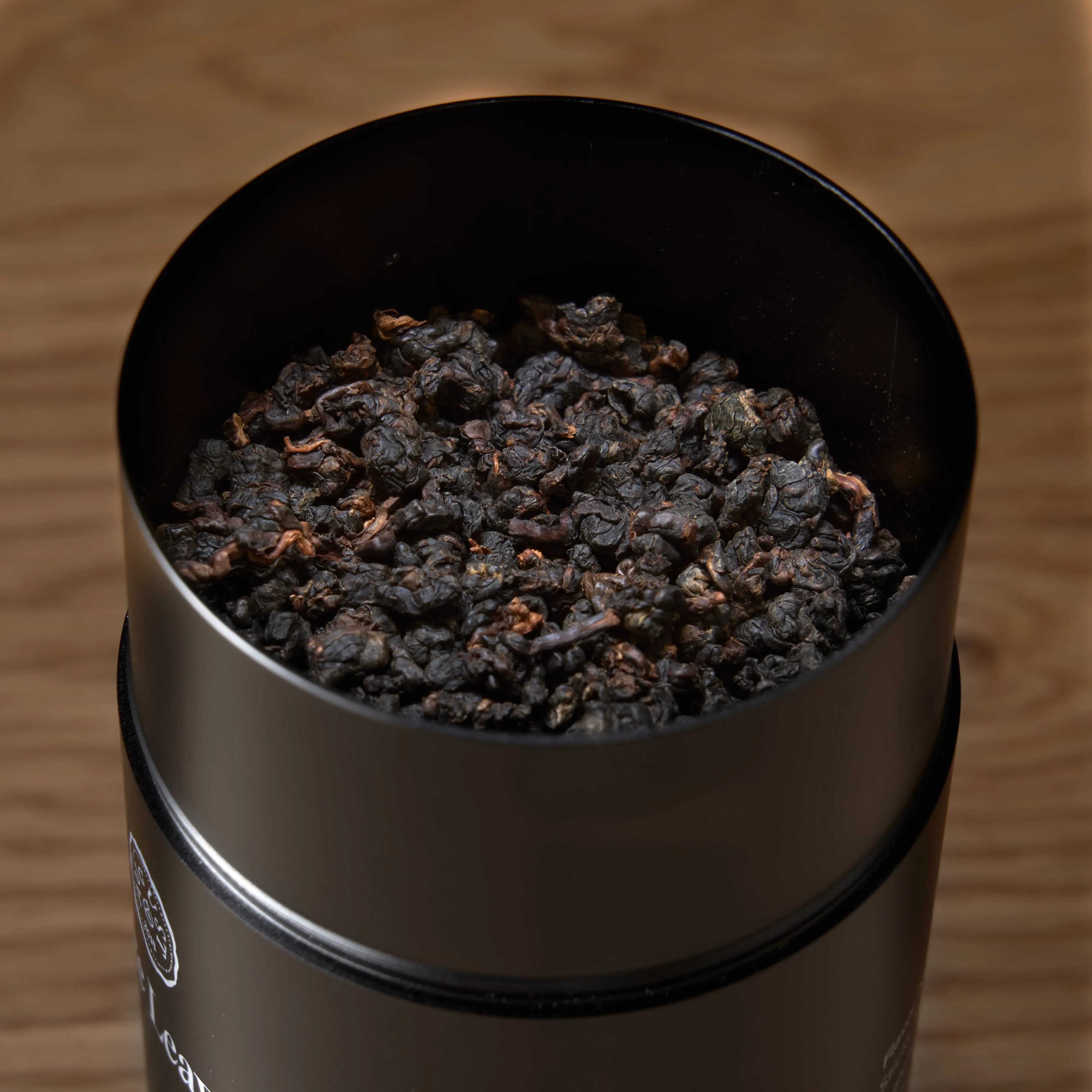 Open cup of Rare Leaves Black Pearl Taiwanese dark roasted oolong tea by August Uncommon Tea, showing rich, dark tea leaves.