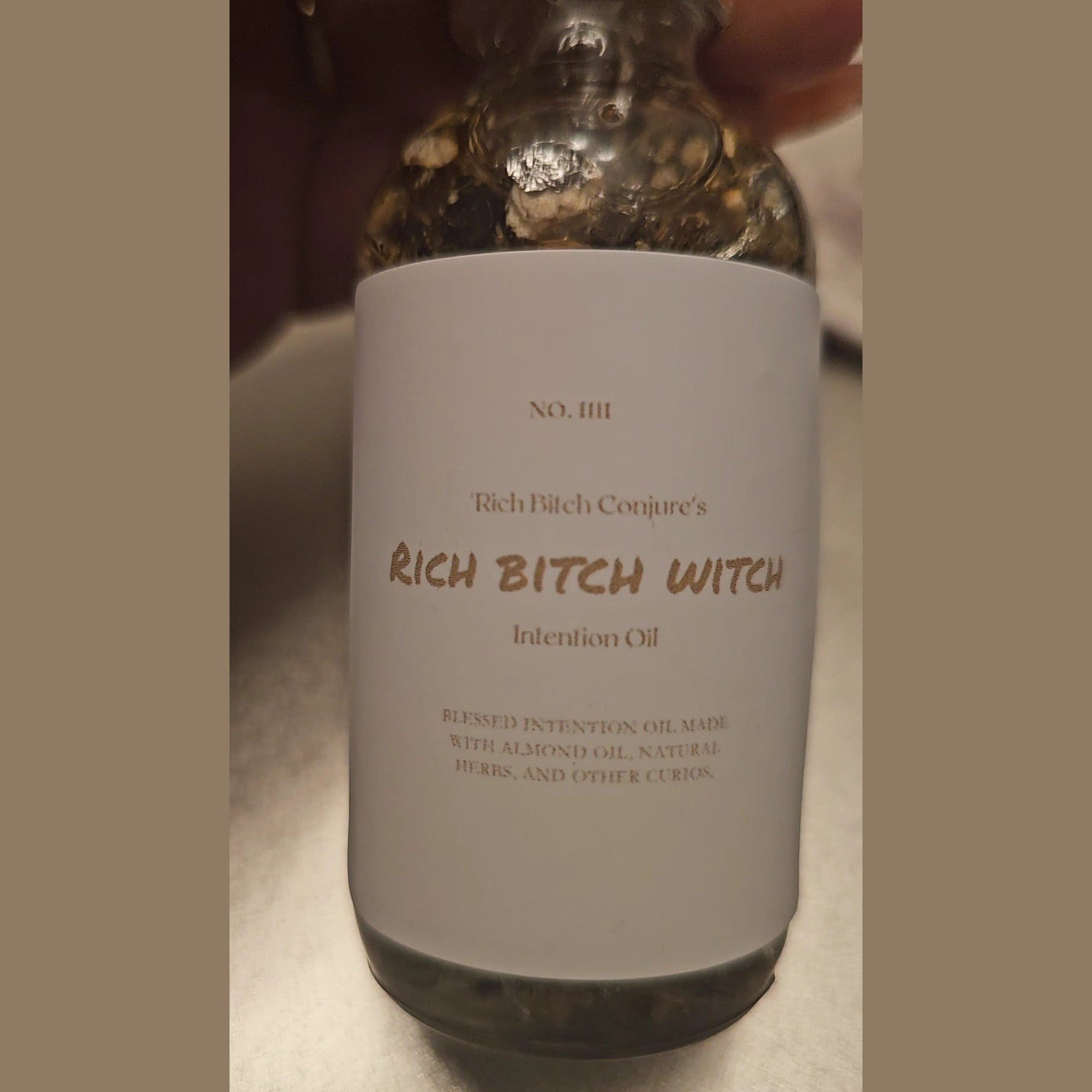 Rich Bitch Conjure Hoodoo oil bottle labeled "Rich Witch Bitch" with a dark, mystical background and decorative elements.