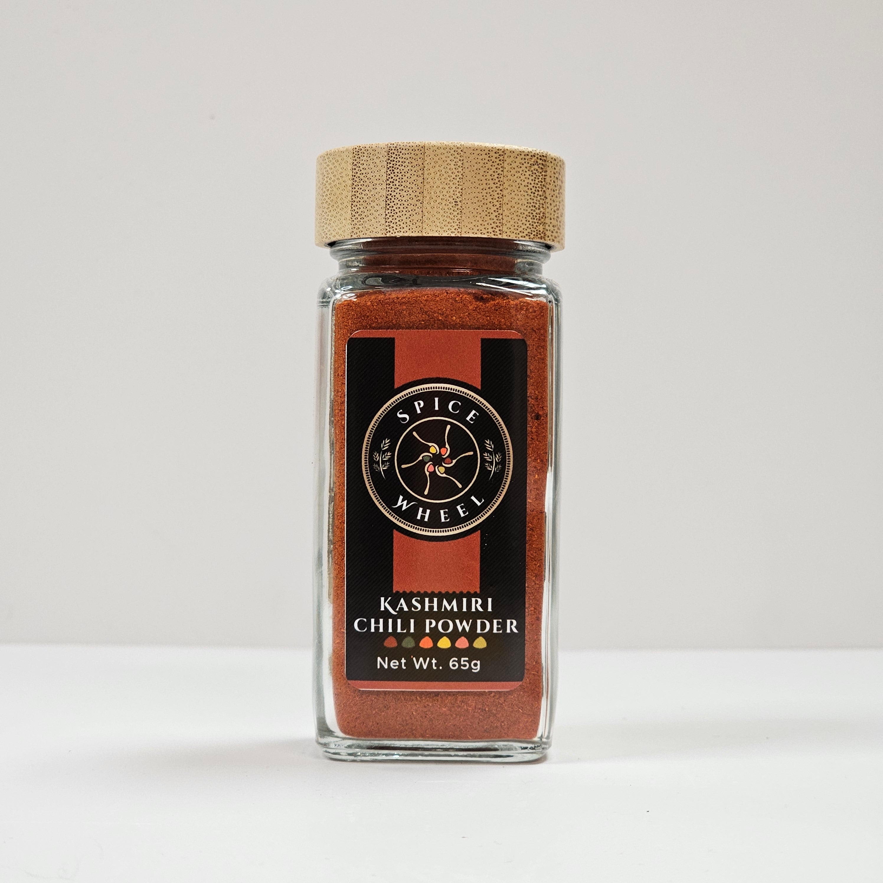 Glass jar of Spice Wheel Kashmiri chili powder with vibrant red chili flakes inside.