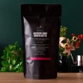 Razzmatazz Raspberry Burnt Sugar Black Tea by August Uncommon Tea in a large 70-cup bag, displayed with tea leaves and packaging.