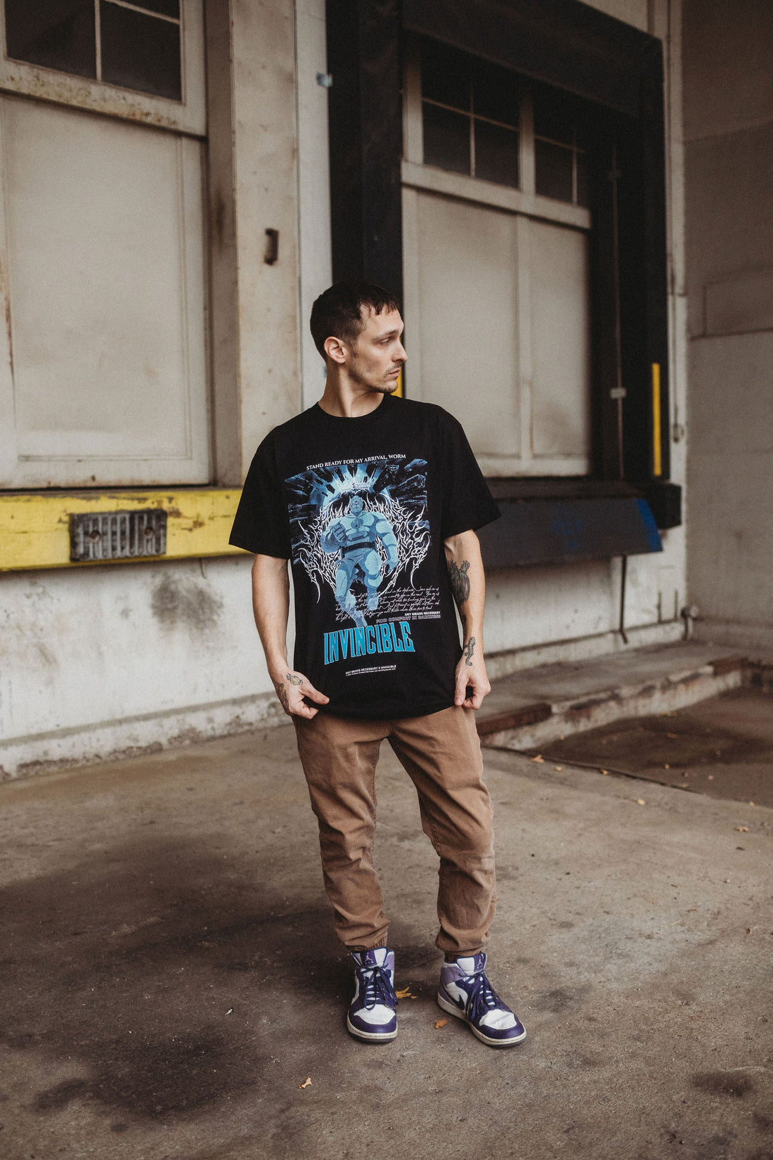 Black Arrival T-Shirt by Any Means Necessary Clothing, featuring a casual fit and graphic design on the front.