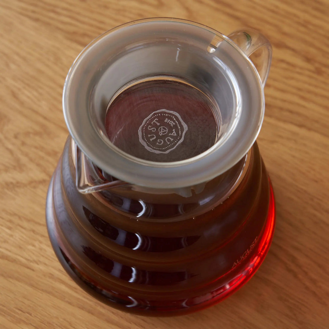 Clear glass two-cup teapot by August Uncommon Tea, showcasing a sleek design for brewing and serving tea.