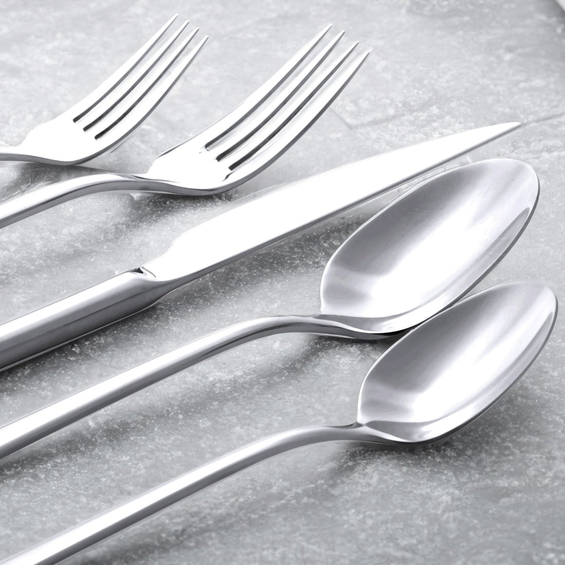 Italic Emilia Mirror 20-piece flatware set with polished stainless steel forks, knives, spoons, and dessert utensils arranged on a table