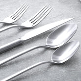 Italic Emilia Mirror 20-piece flatware set with polished stainless steel forks, knives, spoons, and dessert utensils arranged on a table