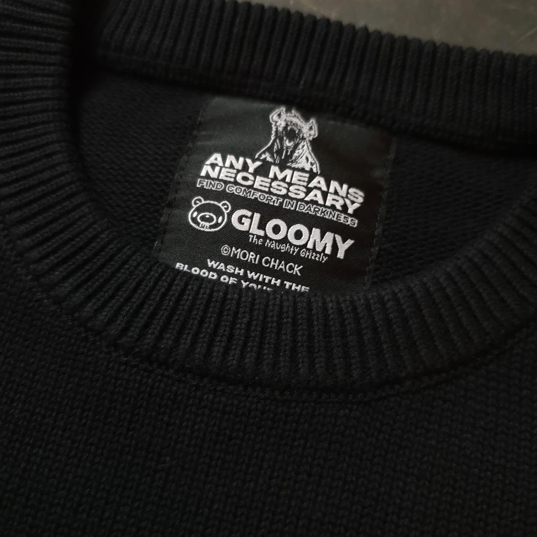 Close-up of the Big Gloomy Knit Sweater from Any Means Necessary Clothing showing its textured, dark-colored knitted fabric.