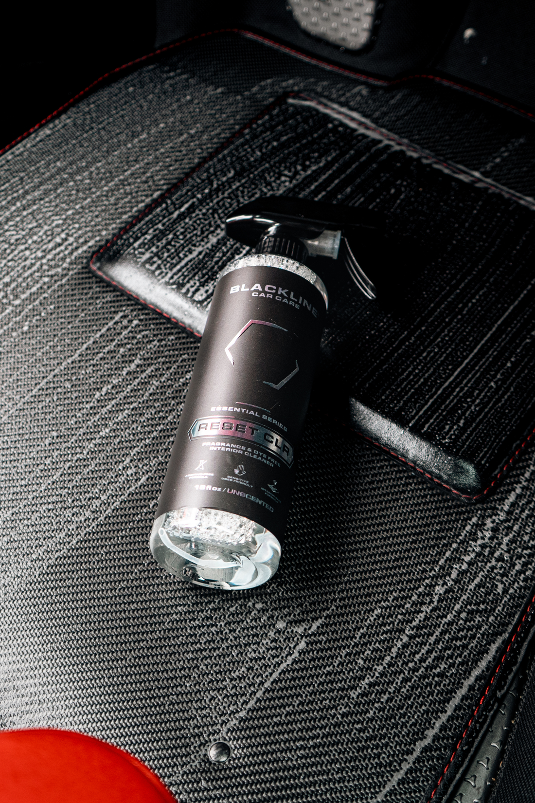 Blackline Car Care RESET interior cleaner and scent booster bottle next to a clean car floor mat on a white background.
