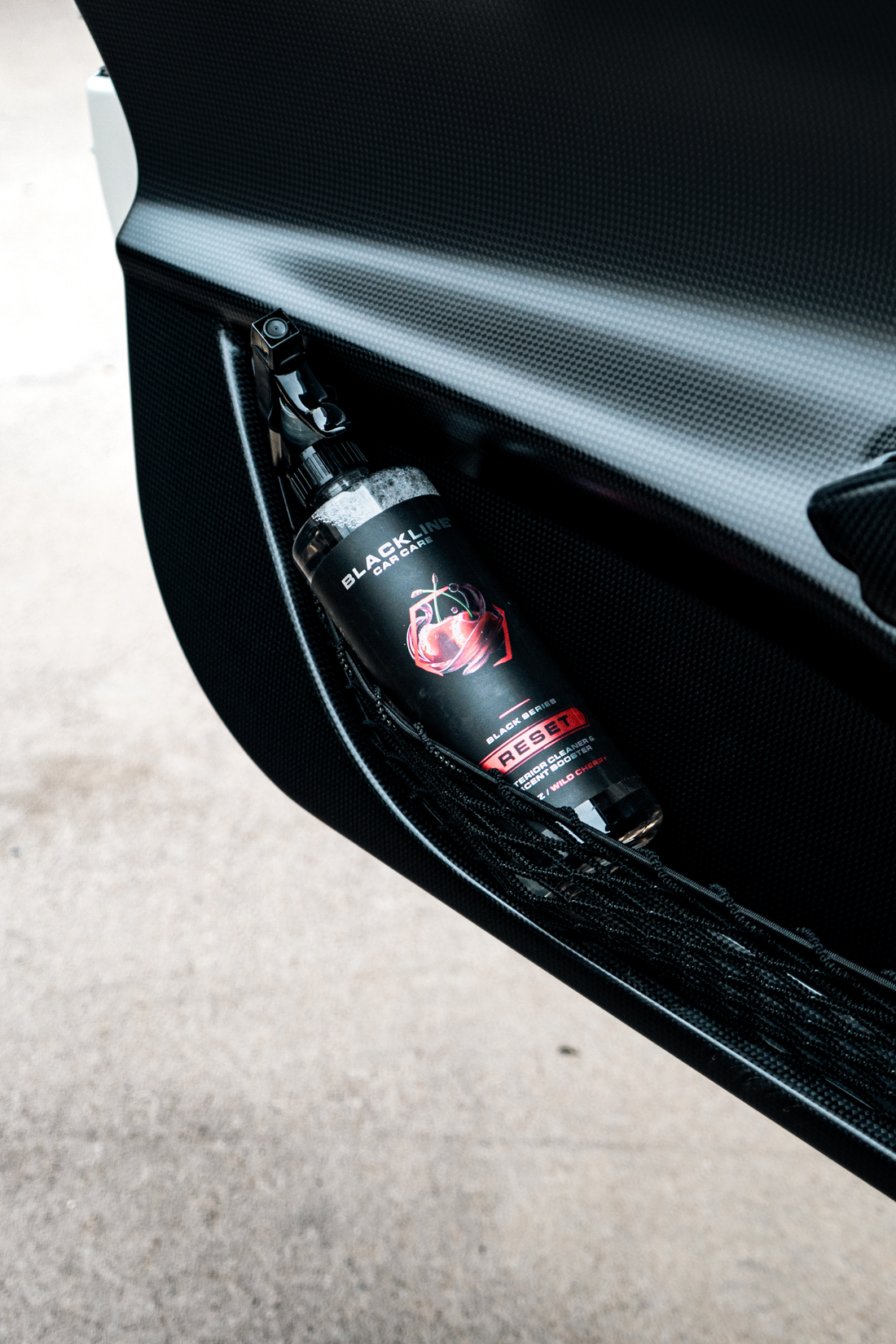 Blackline Car Care BLACKLINE® RESET interior cleaner and scent booster on a car door panel with a wild cherry scent, in a spray bottle.