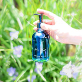 Blue Bloom Botanical Body Oil by Pretty Farm Girl, showing a clear glass bottle with blue floral label and golden cap.
