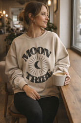 Contemplative woman wearing a Fitkitty Culture Lunar Essence Fleece Crew with moon tribe graphic sweatshirt in a cozy coffee shop setting