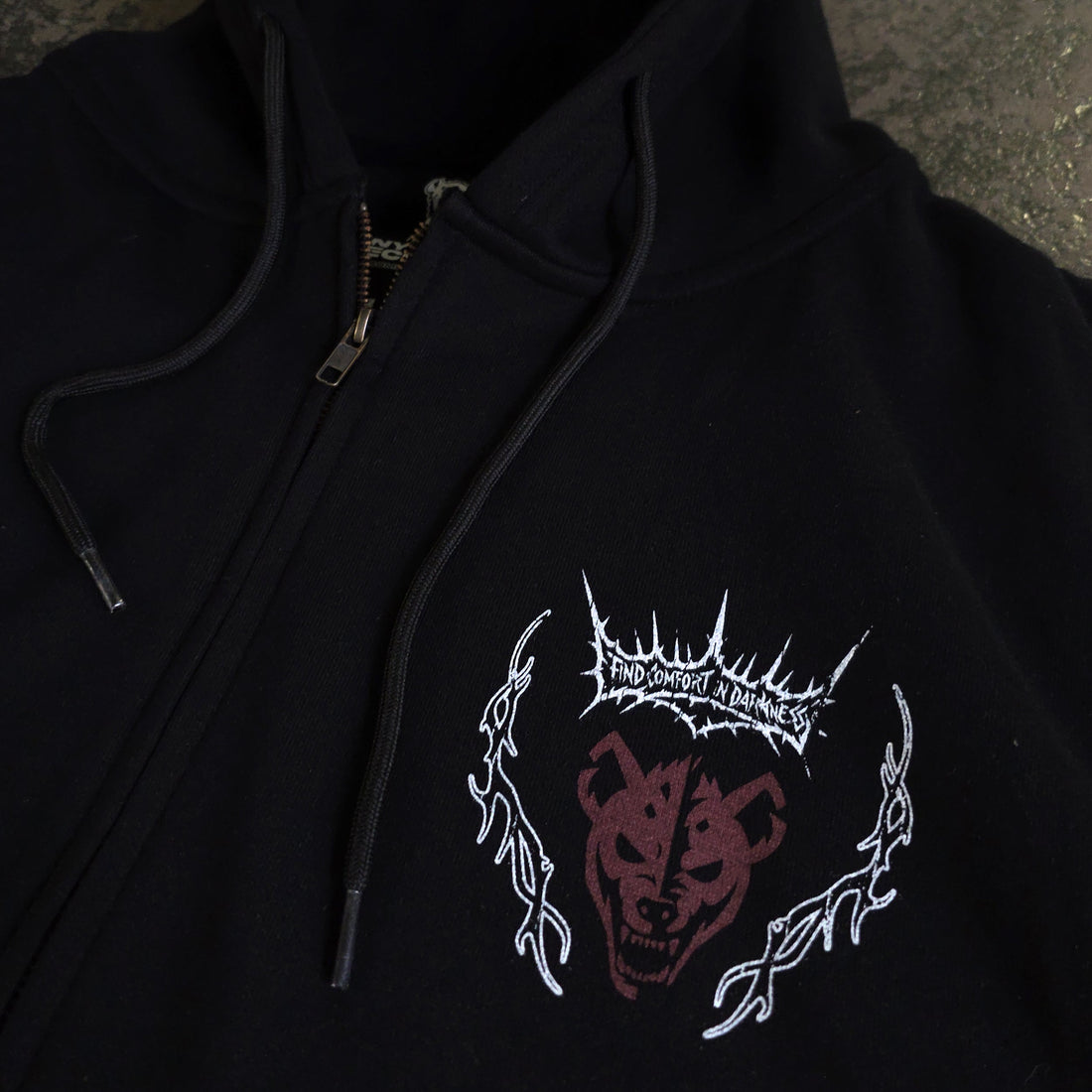 Black Mantra zip-up hoodie by Any Means Necessary Clothing with a front zipper and logo detail, close-up view.