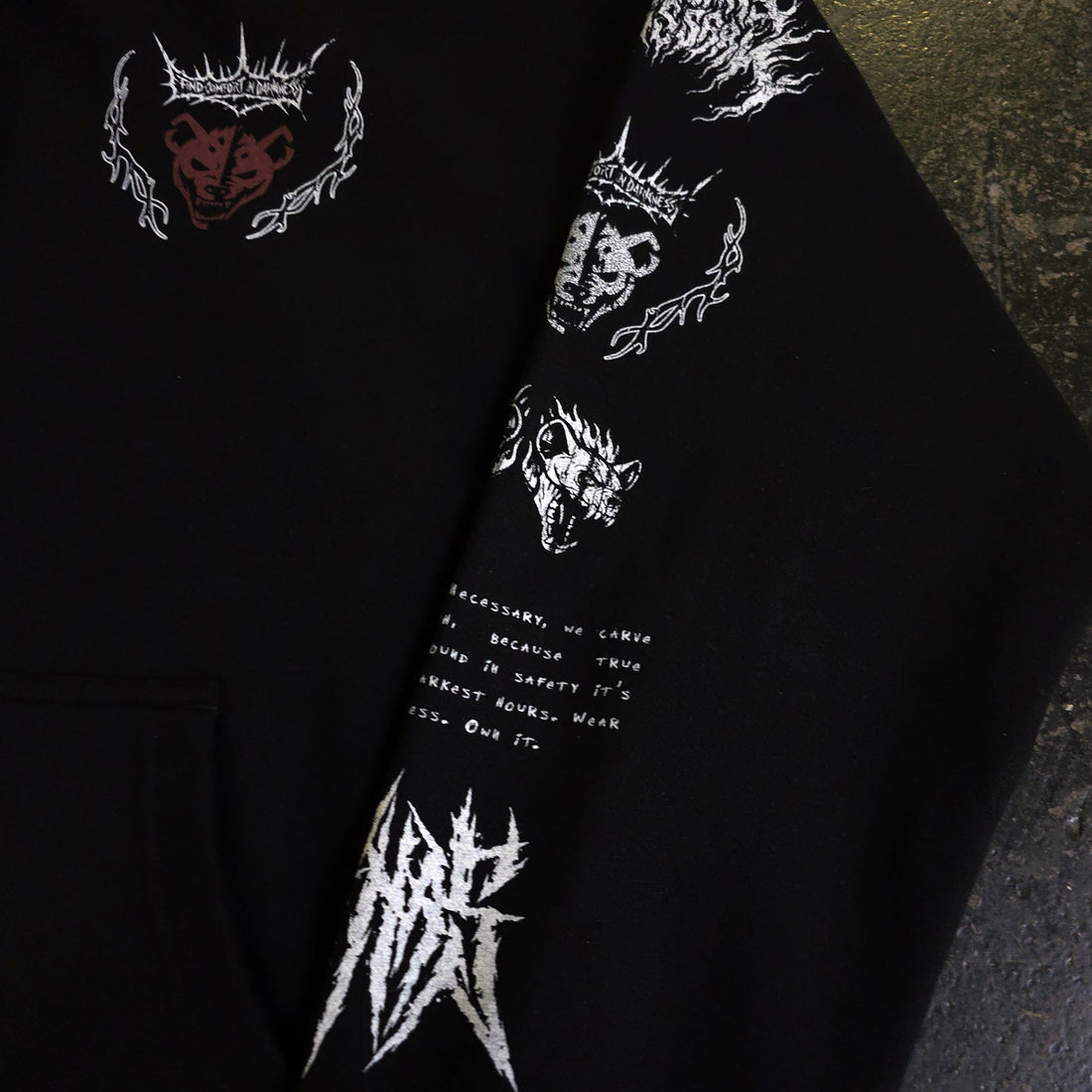 Black Mantra Pullover Hoodie by Any Means Necessary Clothing, close-up view showing the front design and fabric texture.