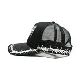Black Thorns Trucker Hat by Any Means Necessary Clothing featuring a front patch and mesh back, shown from side angle.