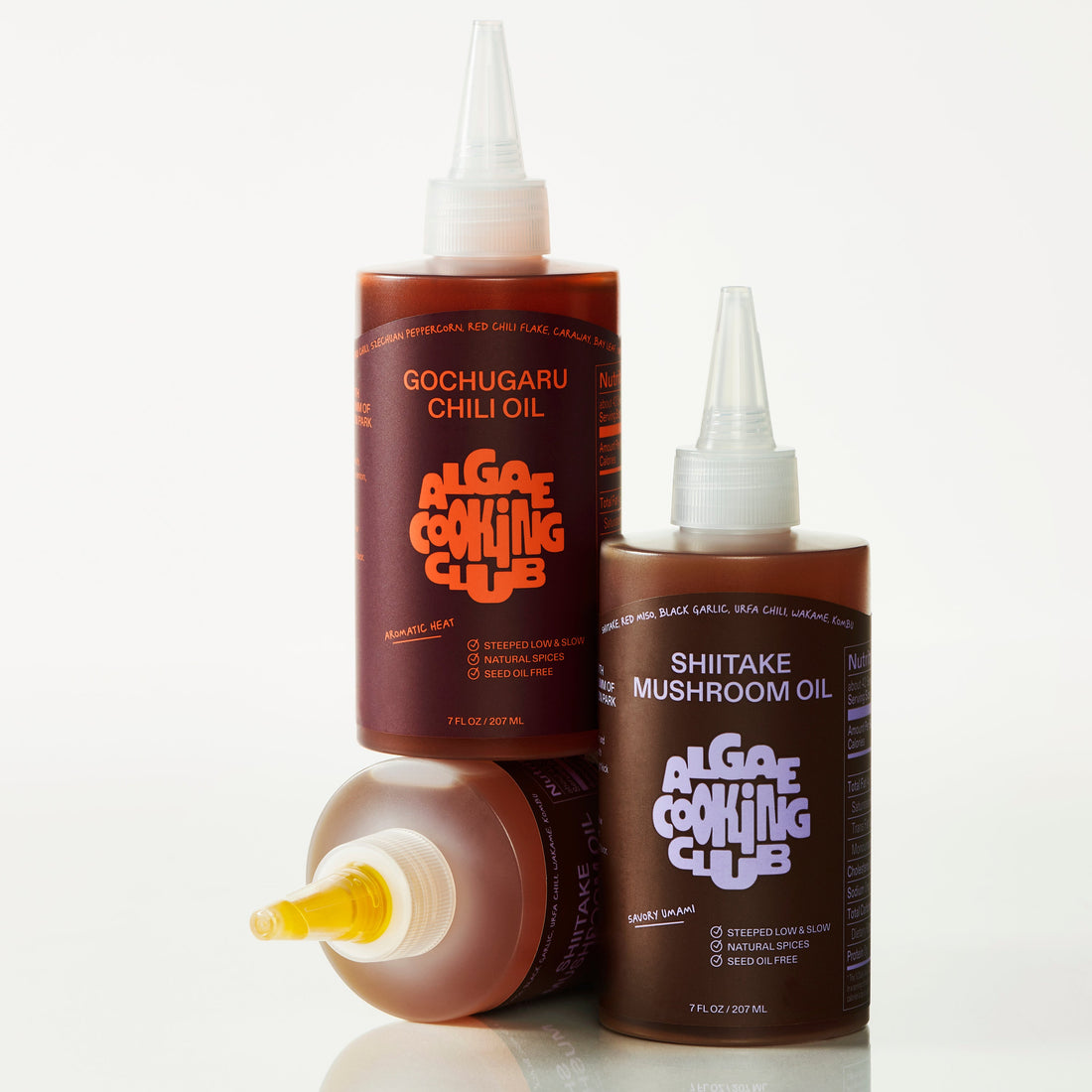 Algae Cooking Club infused oil duo bottles featuring vibrant labels and golden-colored oils on a wooden surface.