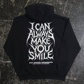 Back view of black Always Smile hoodie by Any Means Necessary Clothing, featuring a smiling face graphic on the back.