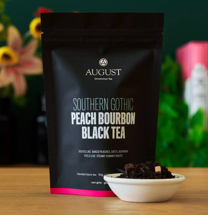 Box of August Uncommon Tea Southern Gothic Peach Bourbon Black Tea in a 15-cup bag, showcasing black tea leaves and packaging.