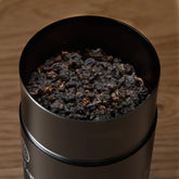 Open cup of Rare Leaves Black Pearl Taiwanese dark roasted oolong tea by August Uncommon Tea, showing rich, dark tea leaves.