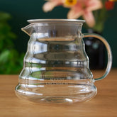 Two cup glass teapot by August Uncommon Tea, showcasing clear glass design and stainless steel lid for brewing tea.