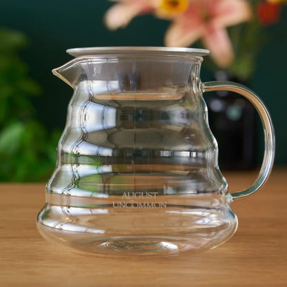 Two cup glass teapot by August Uncommon Tea, showcasing clear glass design and stainless steel lid for brewing tea.