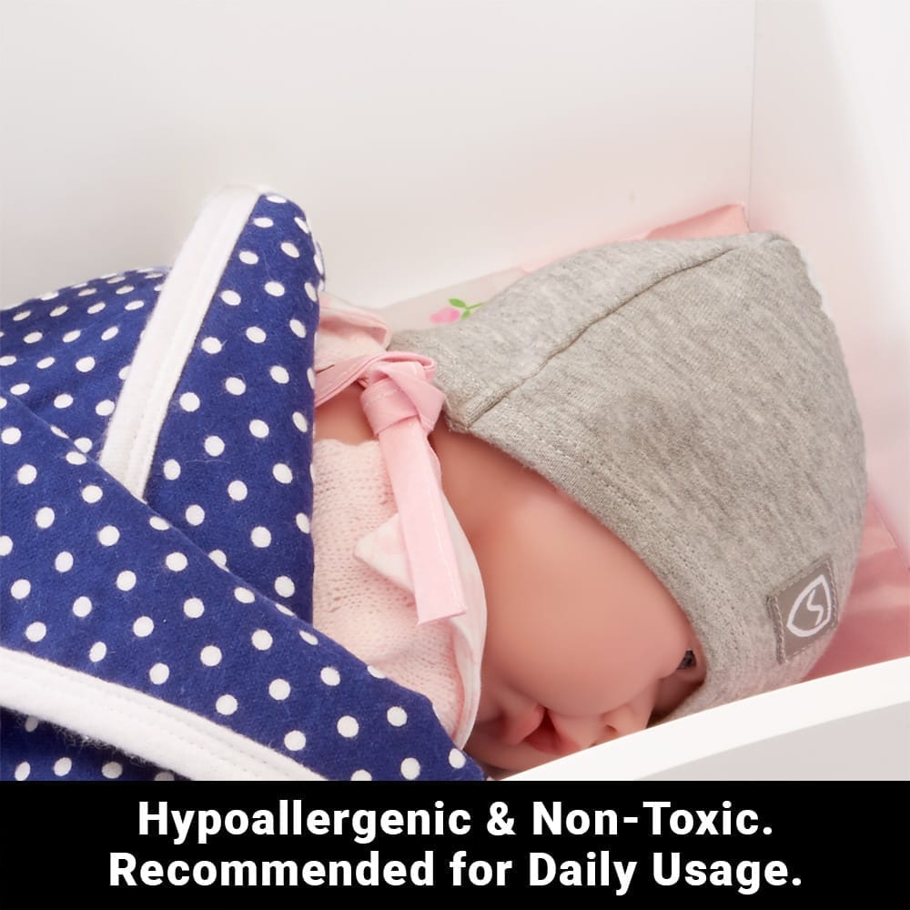 Blue hypoallergenic baby beanie from Shield Your Body, designed for infants and toddlers, shown next to a crib blanket.