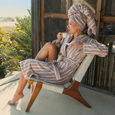Unisex Ultraplush Australian Cotton bathrobe by Italic, soft white fabric with a cozy hood and belt, displayed hanging on a wooden hook.