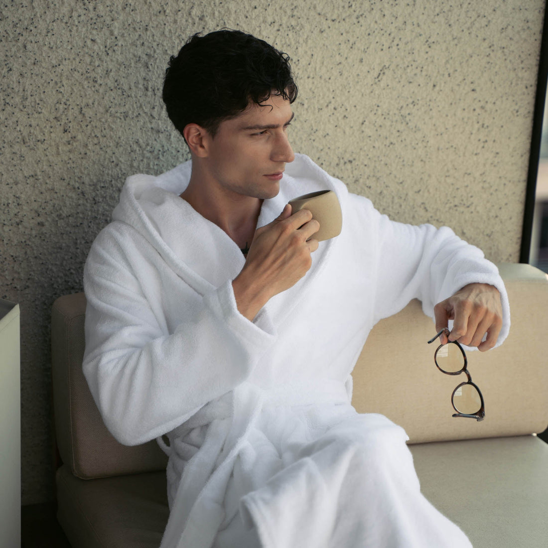 Unisex Ultraplush Australian Cotton bathrobe by Italic, soft white fabric with a tied waist and cozy collar, hanging on a hook.