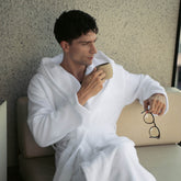 Unisex Ultraplush Australian Cotton bathrobe by Italic, soft white fabric with a tied waist and cozy collar, hanging on a hook.