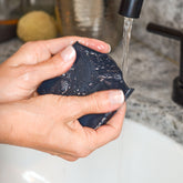 Handmade charcoal tallow and goat milk soap bar from Pretty Farm Girl, shown lathered and resting on a sink.