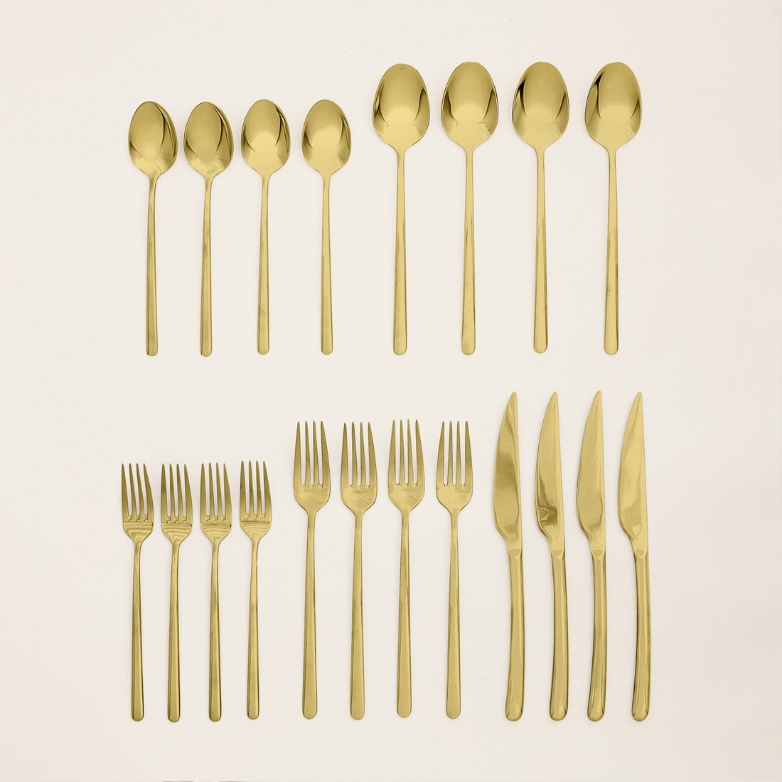 Italic Emilia gold 20-piece flatware set with sleek forks, knives, spoons, and serving pieces on a white background.