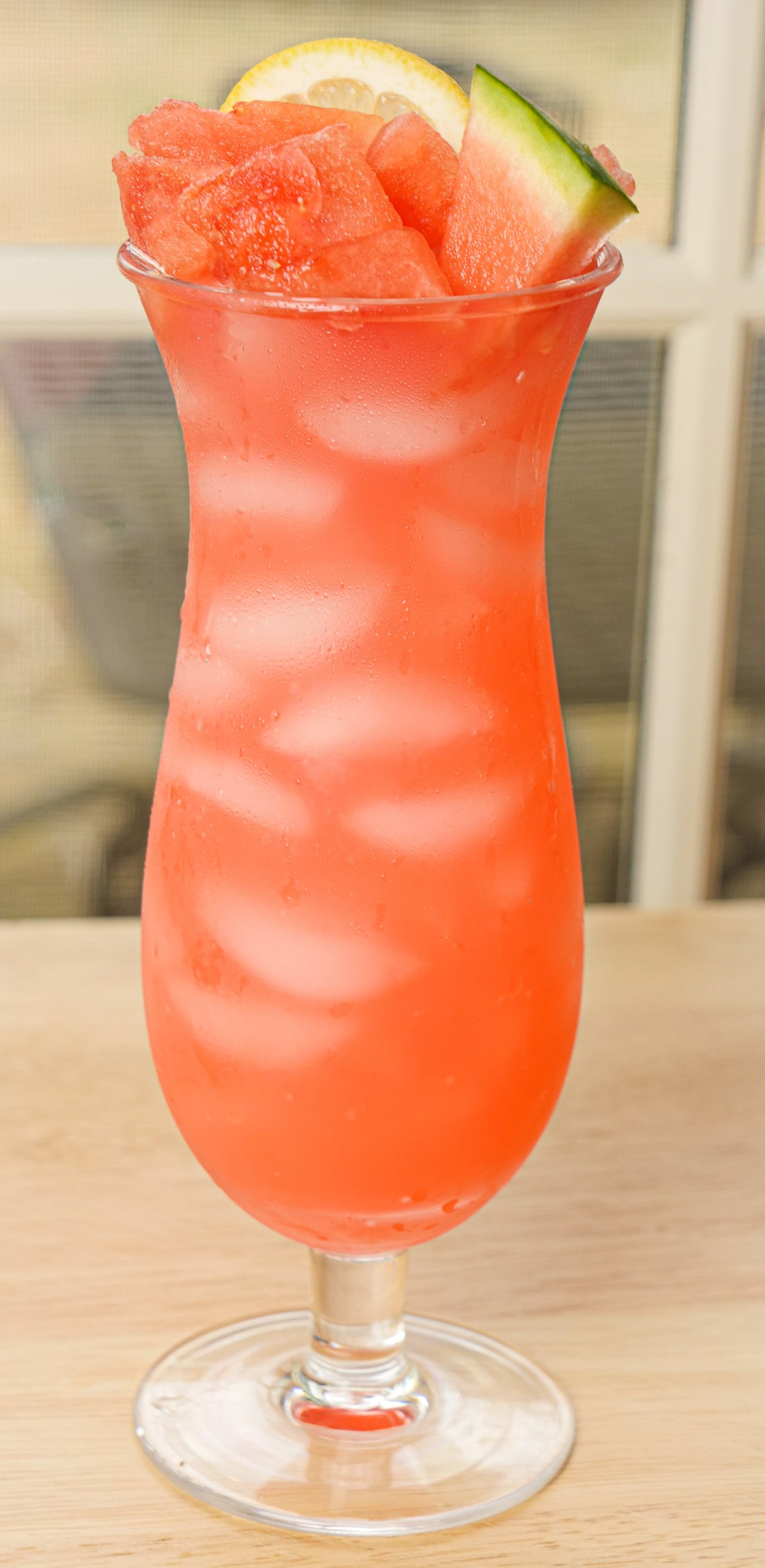 Igotchu Watermelon Lemonade juice in a clear glass with fresh watermelon and lemon slices on a wooden table.