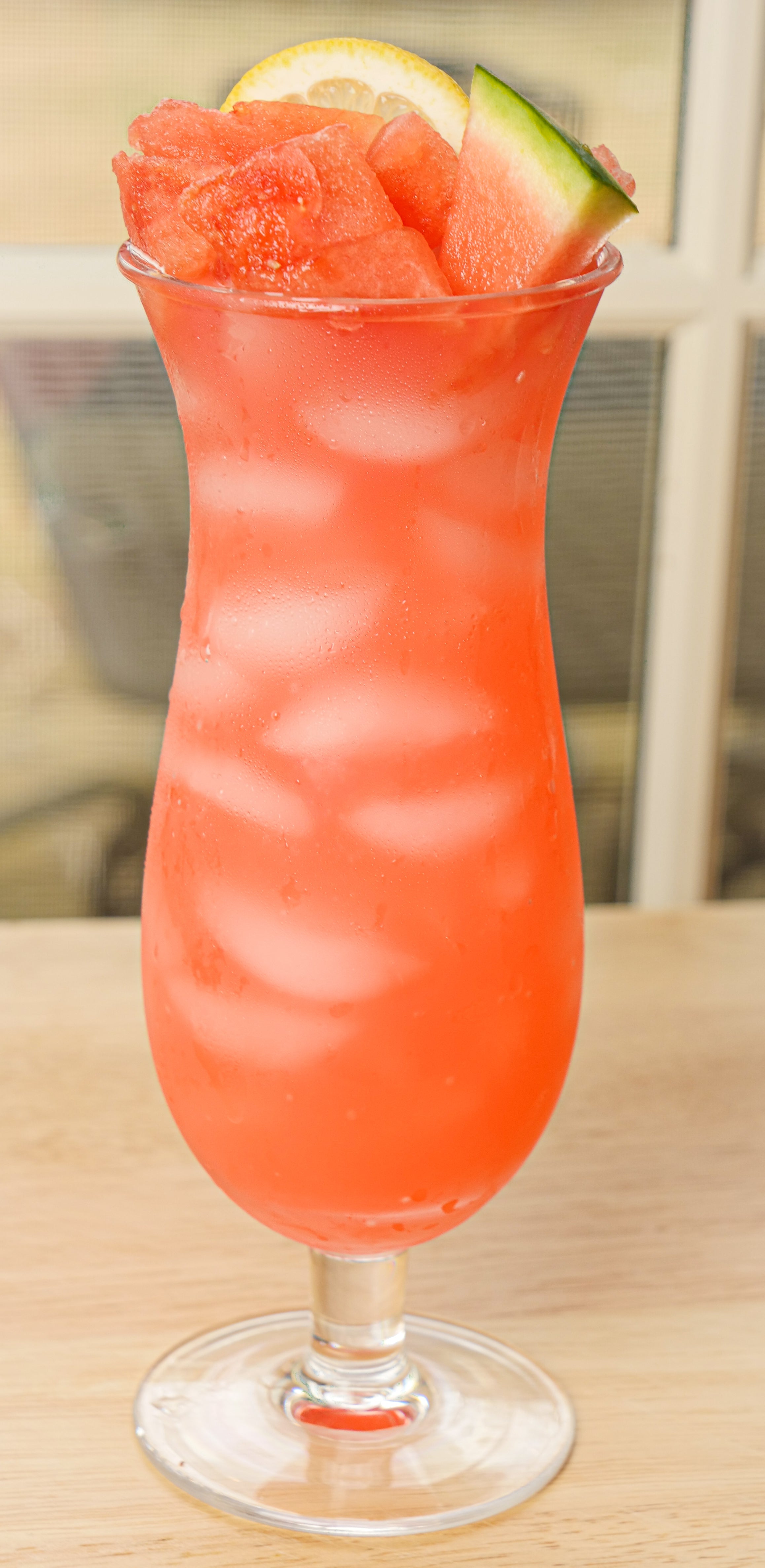Igotchu Watermelon Lemonade juice in a clear glass with fresh watermelon and lemon slices on a wooden table.