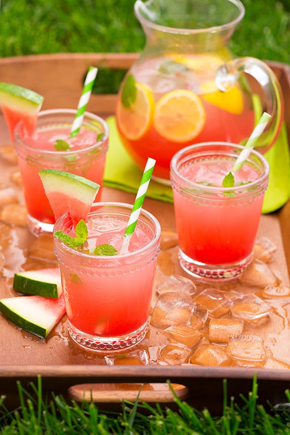 Igotchu Watermelon Lemonade juice in a clear glass, showing vibrant pink liquid with a fresh watermelon and lemon garnish.