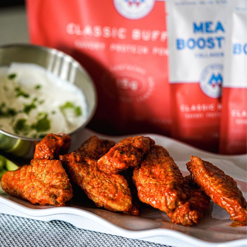 Creamy buffalo chicken wings with Collagen+ Protein Blend from Meal Boosters protein powder packaging.