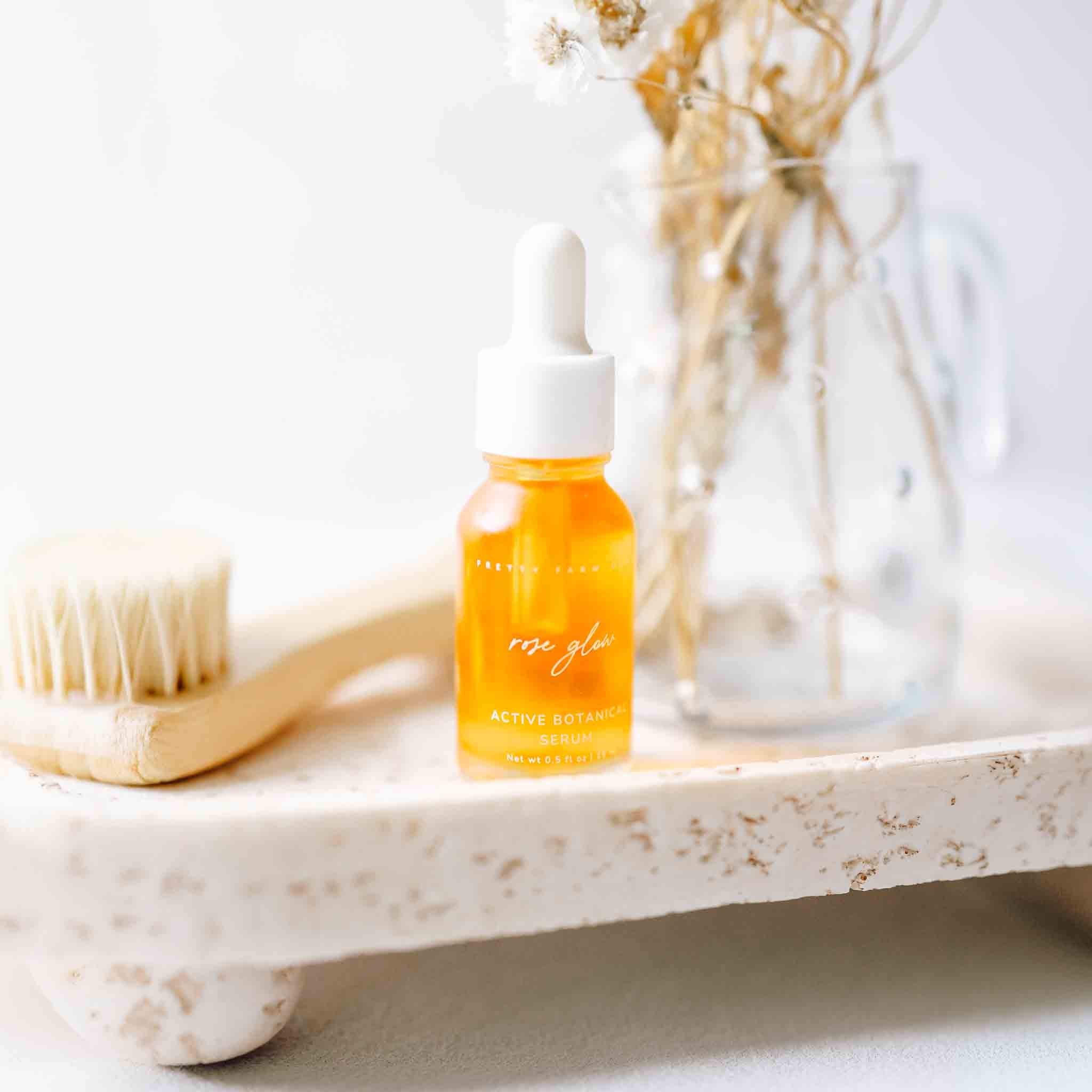 Pretty Farm Girl Rose Glow Anti-Aging Face Serum in a sleek bottle with rose petals around, highlighting natural ingredients.