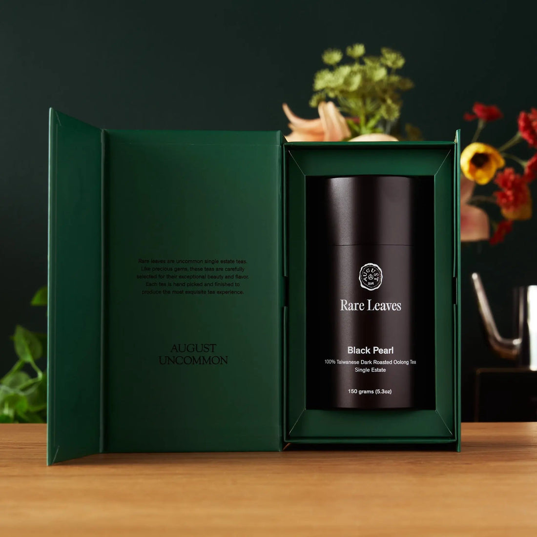 Open box of Rare Leaves Black Pearl Taiwanese dark roasted oolong tea by August Uncommon Tea, showing twisted dark tea leaves inside.