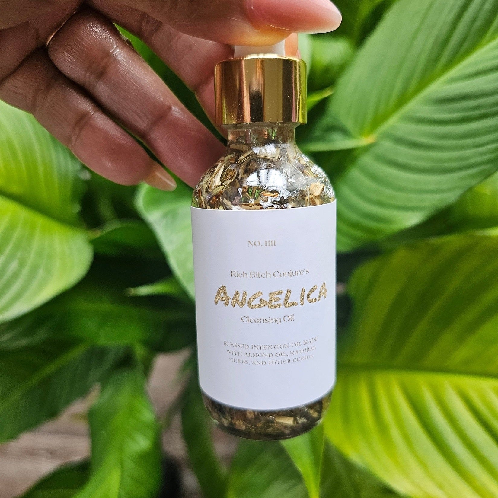 Rich Bitch Conjure Angelica Cleansing Oil in a bottle, part of Hoodoo Oils by Rich Bitch Conjure, with herbal ingredients visible.