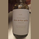 Rich Bitch Conjure Hoodoo oil bottle labeled "Rich Witch Bitch" with a dark, mystical background and decorative elements.