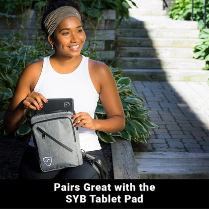 Woman sitting outside, placing a tablet pad into a Shield Your Body SYB Sling Bag, a stylish backpack for everyday use.