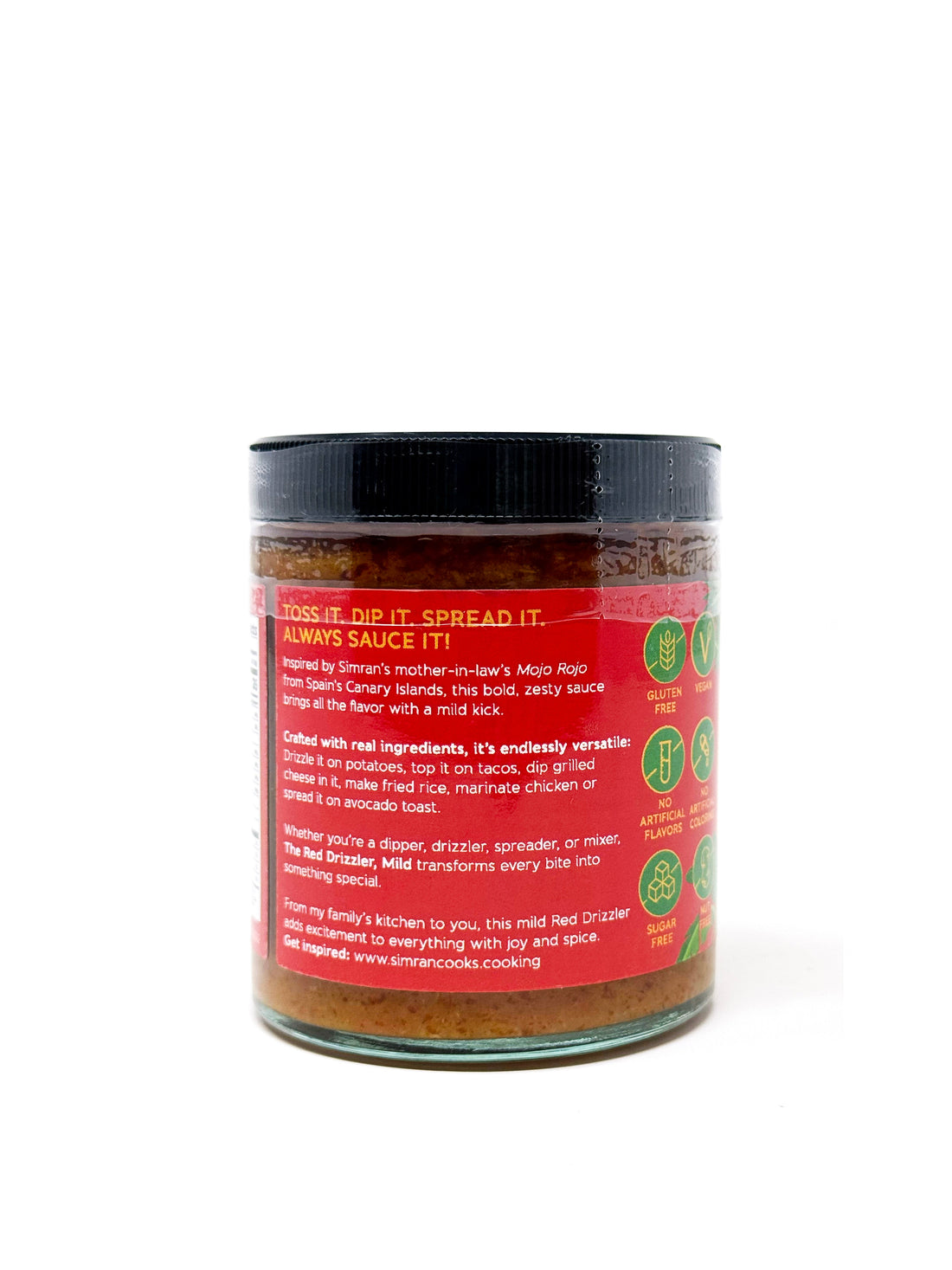 The Red Drizzler Mojo Rojo mild sauce in a clear glass jar with a red label, featuring a spoon drizzling the vibrant red sauce.
