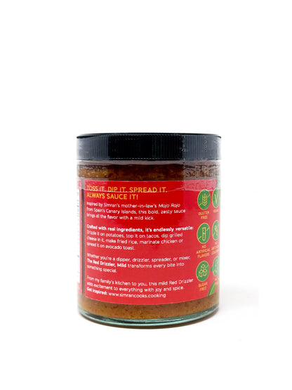 The Red Drizzler Mojo Rojo mild sauce in a clear glass jar with a red label, featuring a spoon drizzling the vibrant red sauce.