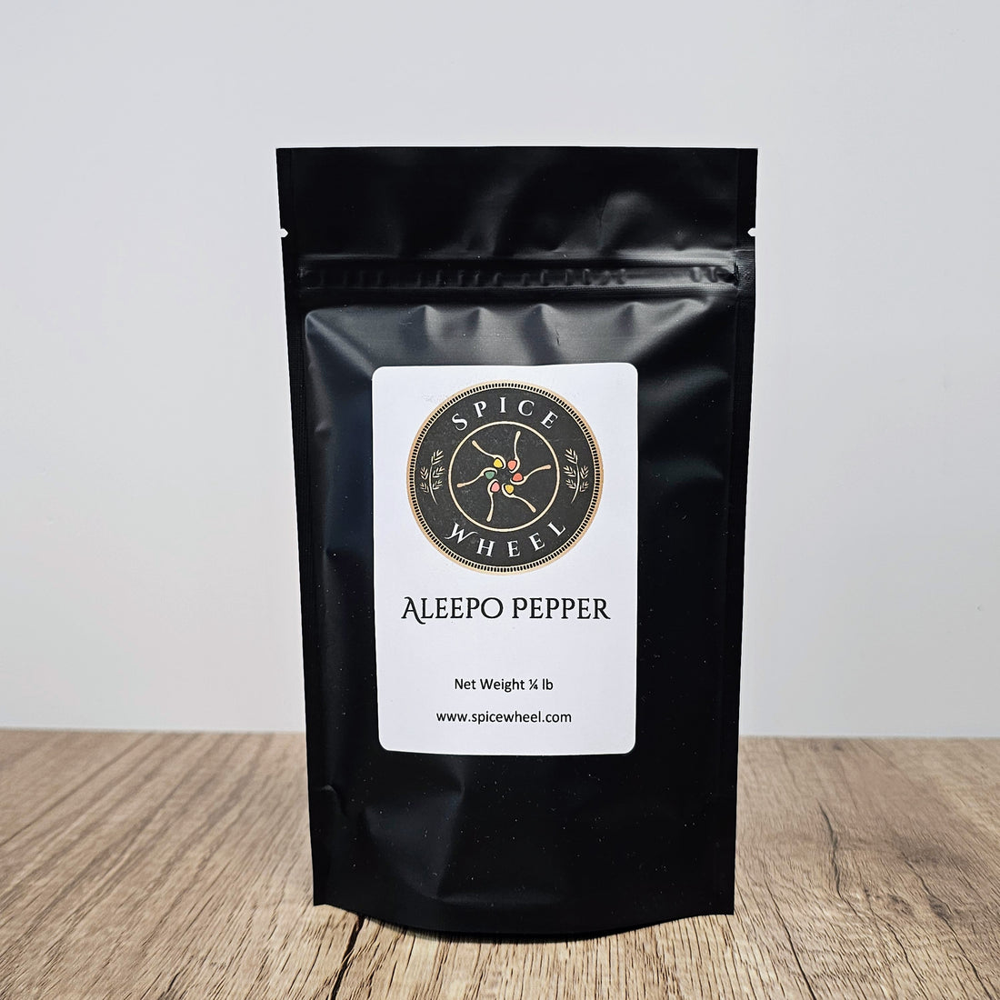 A 1/4 lb package of Aleepo Pepper from Spice Wheel, a vibrant bulk spice with red and green peppercorns in a clear container.