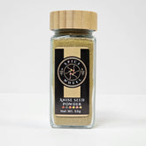 Fine greenish-brown anise seed powder in a clear glass jar from Spice Wheel, showing its smooth texture and aromatic quality.
