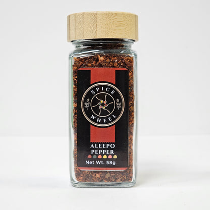 Glass jar of Aleepo Pepper from Spice Wheel, filled with vibrant, whole red peppers in a clear container on a white background.