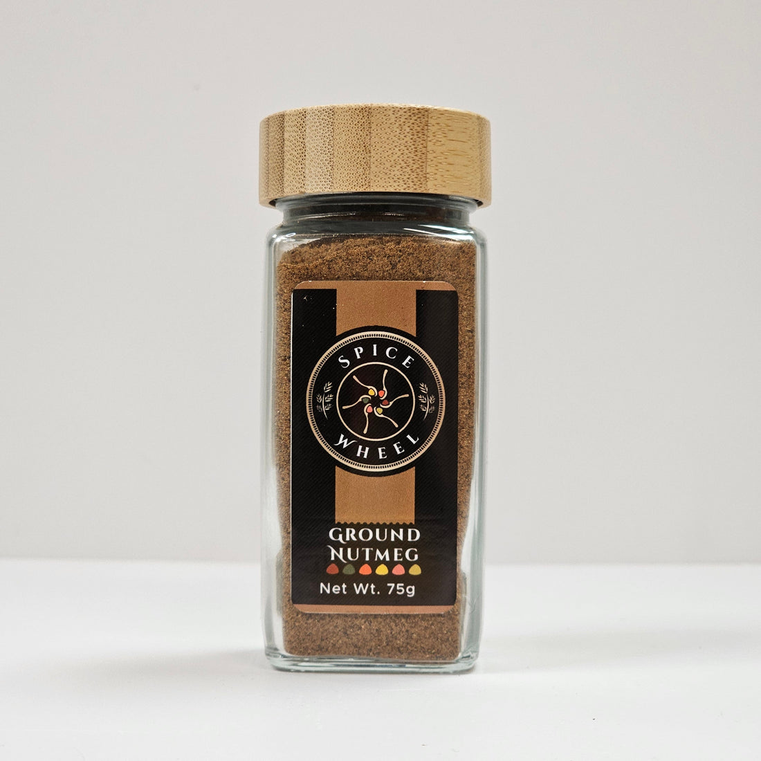 Ground nutmeg in a glass jar by Spice Wheel, showing finely ground spice with a textured surface inside the clear container.