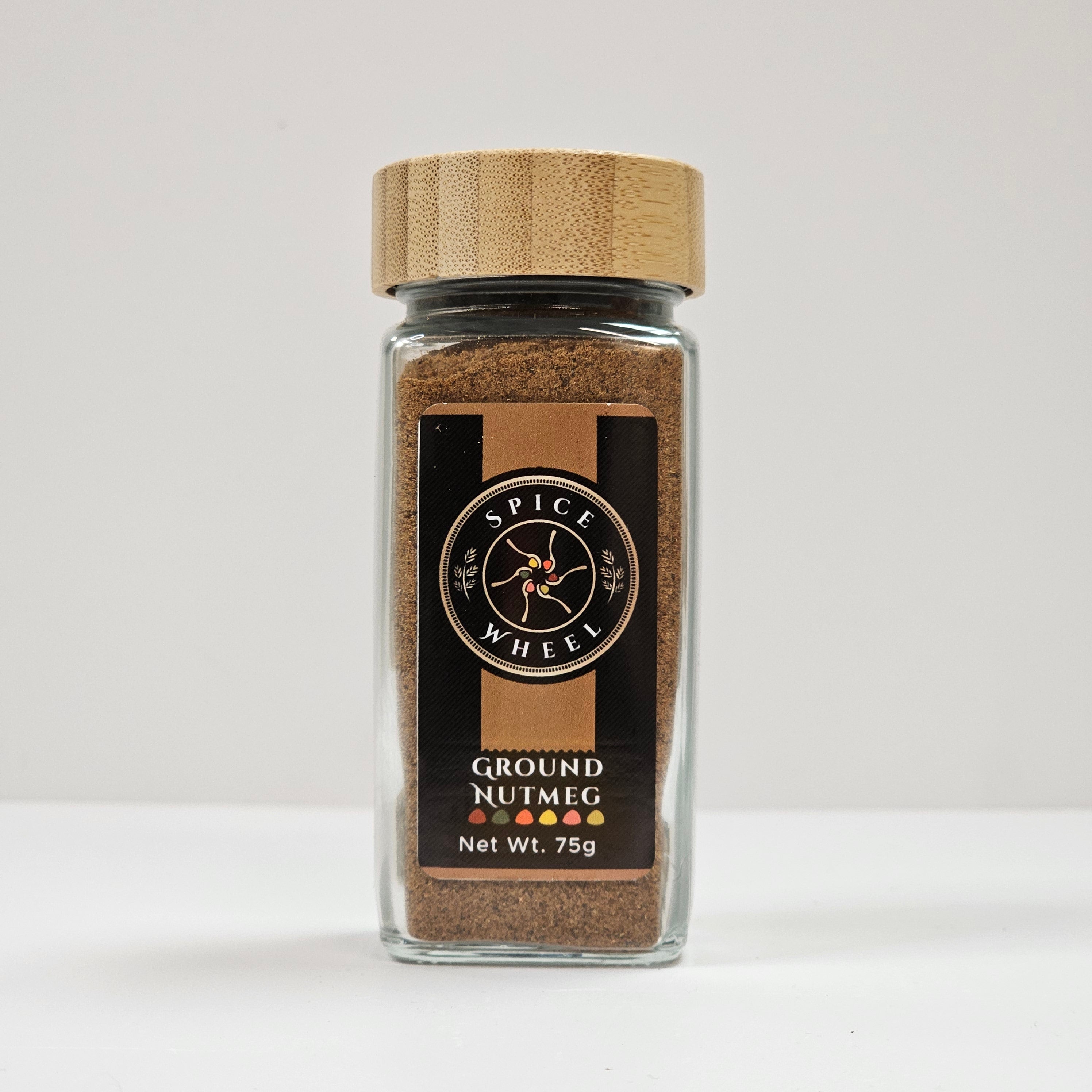 Ground nutmeg in a glass jar by Spice Wheel, showing finely ground spice with a textured surface inside the clear container.