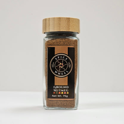 Ground nutmeg in a glass jar by Spice Wheel, showing finely ground spice with a textured surface inside the clear container.