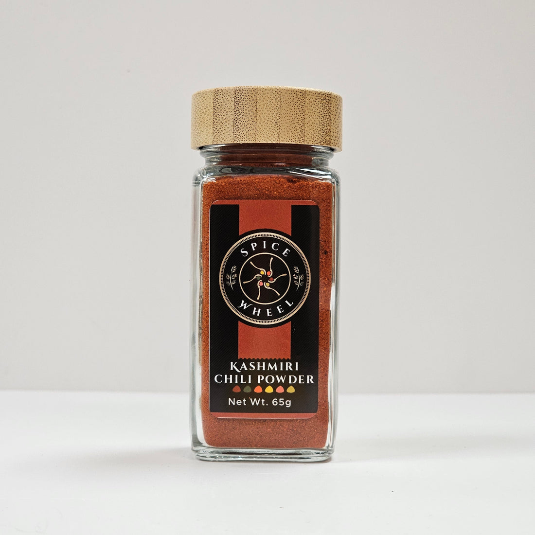 Glass jar of Spice Wheel Kashmiri chili powder with vibrant red chili flakes inside.