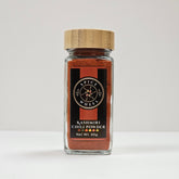 Glass jar of Spice Wheel Kashmiri chili powder with vibrant red chili flakes inside.