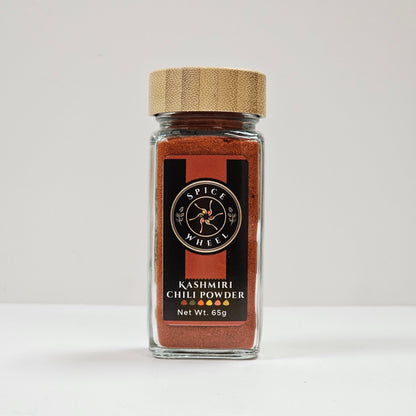 Glass jar of Spice Wheel Kashmiri chili powder with vibrant red chili flakes inside.