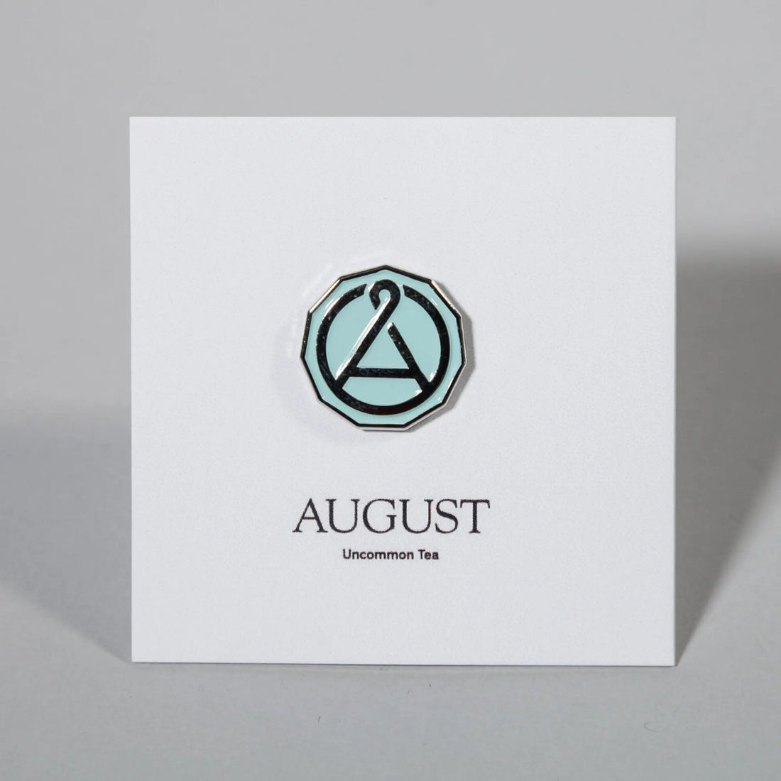 August Seal enamel pin featuring the August Uncommon Tea logo, with a colorful, detailed design on a swag-style pin.