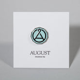August Seal enamel pin featuring the August Uncommon Tea logo, with a colorful, detailed design on a swag-style pin.